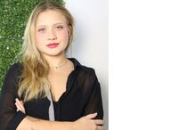 Mulher loira posa com camisa preta, braços cruzados e tatuagem