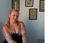 Mulher posa com tatuagens nos braços e pinturas de história natural na parede