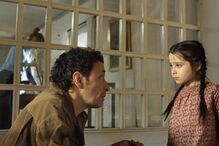 Um homem fala com uma menina com tranças perto de uma janela