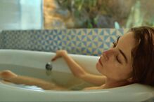 Mulher relaxa numa banheira com azulejos azuis e brancos