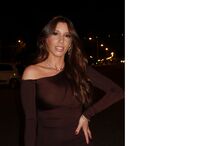 Mulher posa com vestido castanho e joias sob luzes da cidade