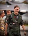 Piloto sorri junto a dois homens e um avião militar