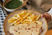 Prato com bife, molho, pimenta rosa e batatas fritas, servido por um empregado de mesa