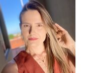 Mulher posa com um vestido castanho e um colar, sob a luz solar