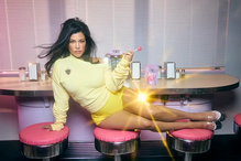 Kourtney Kardashian posa num cenário retro com roupa amarela e um chupa-chupa