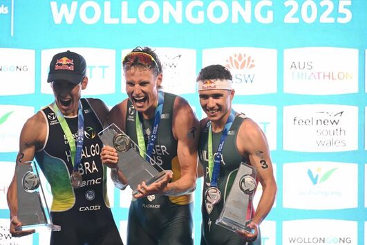 Matthew Hauser, da Austrália, comemora o primeiro lugar, ao lado do segundo colocado Miguel Hidalgo (à esquerda), do Brasil, e do terceiro colocado Vasco Vilaca (à direita), de Portugal, no Campeonato Mundial de Triatlo em Wollongong, Austrália, em 19 de outubro de 2025.
