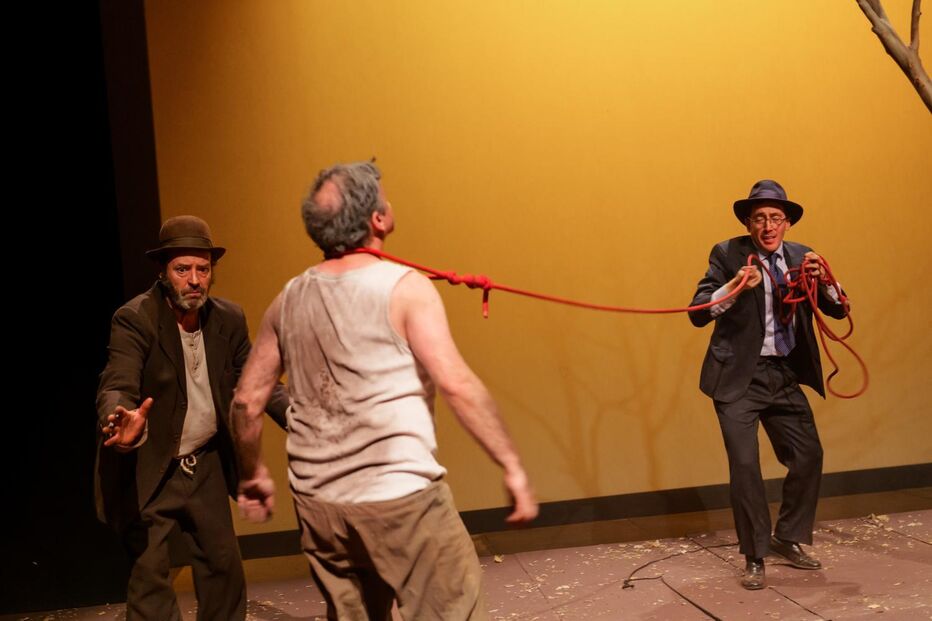 Atores numa peça de teatro com um homem amarrado a uma corda