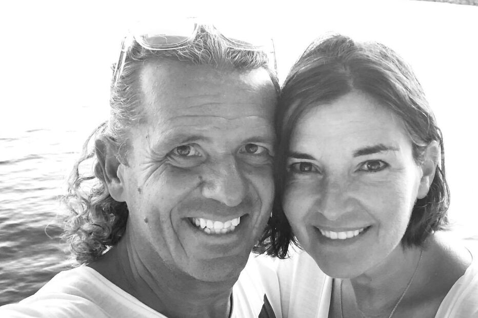 Um casal sorri para a câmara com uma paisagem costeira ao fundo