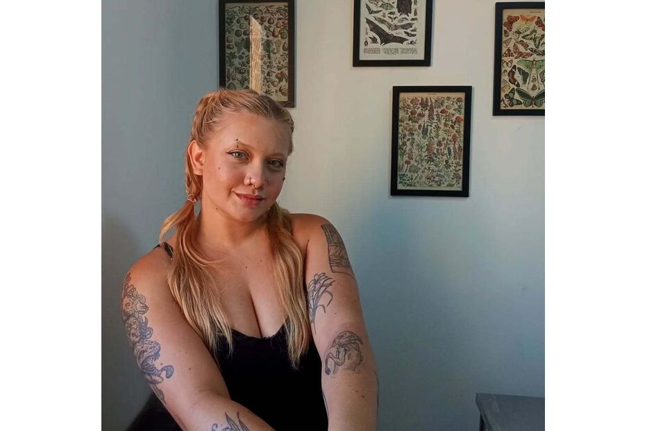 Mulher posa com tatuagens nos braços e pinturas de história natural na parede