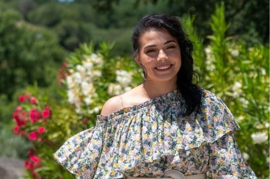 Catarina Manique sorri com vestido floral em cenário natural.
