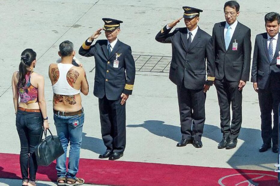 Monarca tailandês surge com a companheira, enquanto é cumprimentado por oficiais