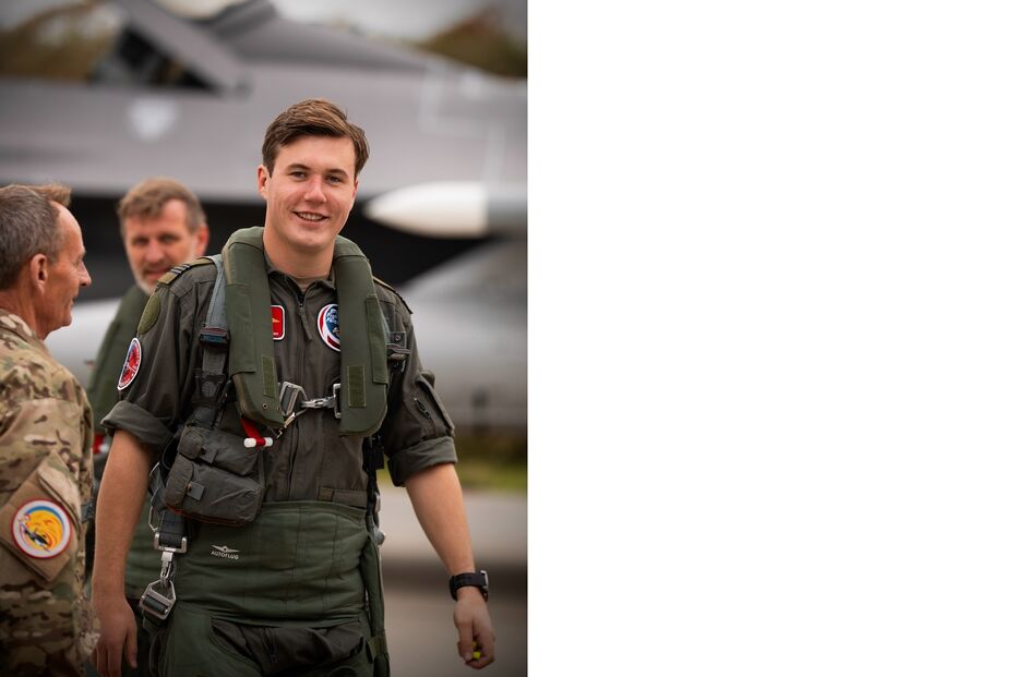 Piloto sorri junto a dois homens e um avião militar