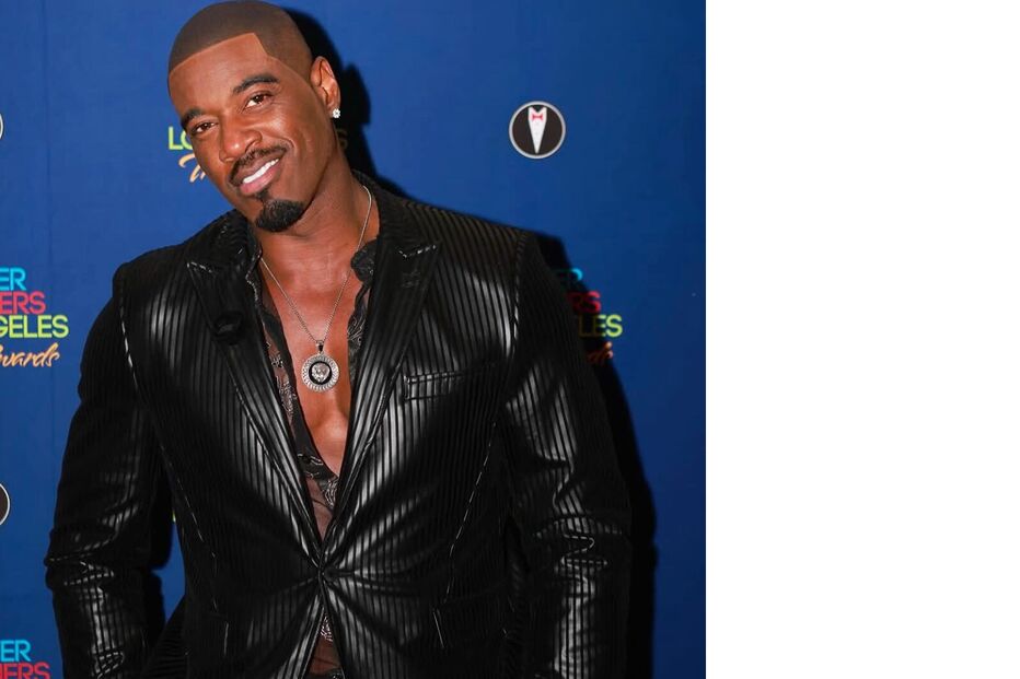 Homem sorri num evento com fato preto brilhante e colar