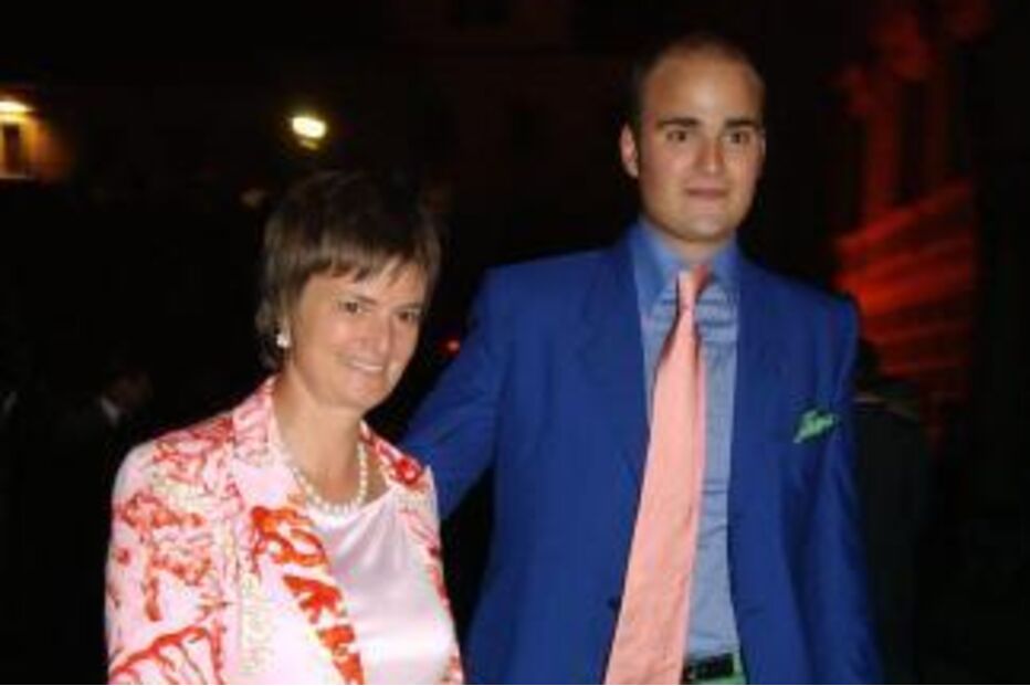 Homem de fato azul e calças verdes acompanha mulher de saia laranja