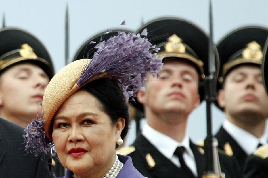 Mulher com um chapéu roxo e colar de pérolas rodeada por militares