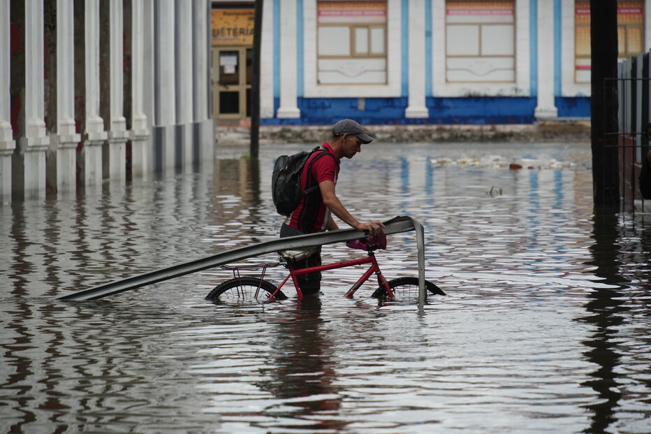 Homem atravessa rua alagada com bicicleta