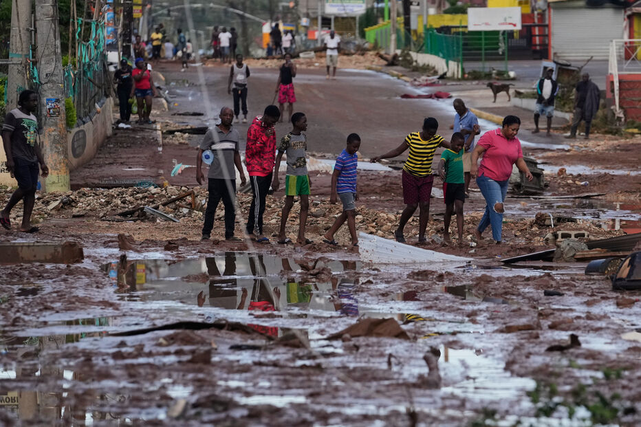 Após a tempestade, moradores atravessam rua inundada com destroços