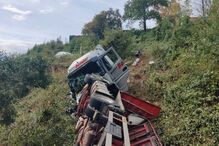 Camião tombado numa encosta com vegetação densa junto a uma estrada