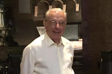 Homem sorri em frente a uma parede de tijolos com arcos