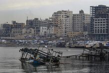 Destruição em Gaza após conflito, com prédios danificados e barcos naufragados
