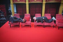 Dois homens em cadeiras num cenário de palco