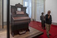 Homem observa piano antigo em exposição com a frase 