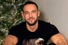 Homem sorri para a câmara junto a uma árvore decorada