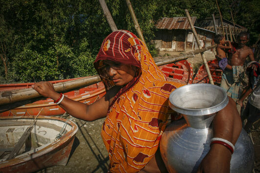 Mulher transporta água no Bangladesh, onde a Igreja Católica investe em saúde e educação