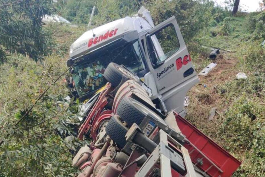 Camião tombado numa ravina, com danos visíveis na cabine e na carga