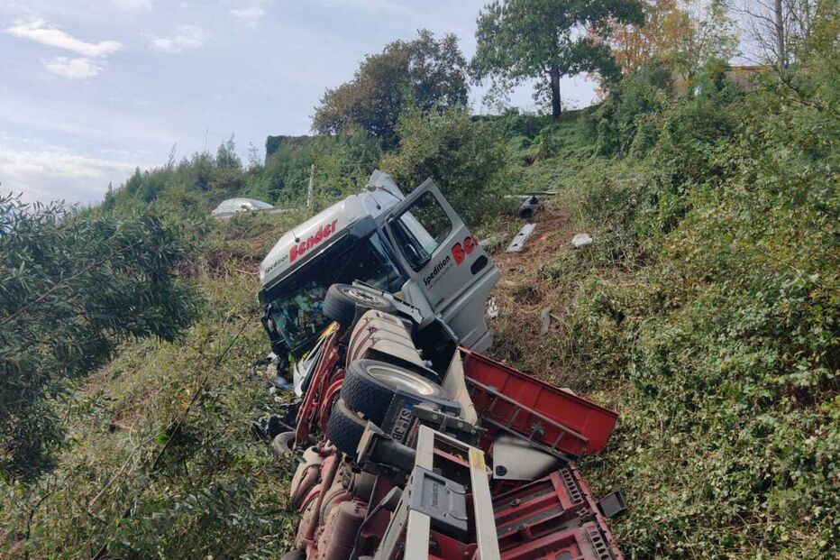 Camião tombado numa encosta com vegetação densa junto a uma estrada