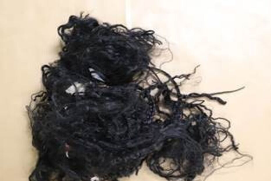 Emaranhado de cabelo escuro junto a uma régua amarela, possivelmente evidência forense.
