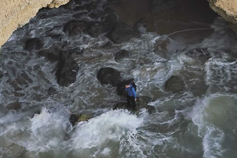 Um homem está em pé sobre rochas na água perto de uma gruta costeira