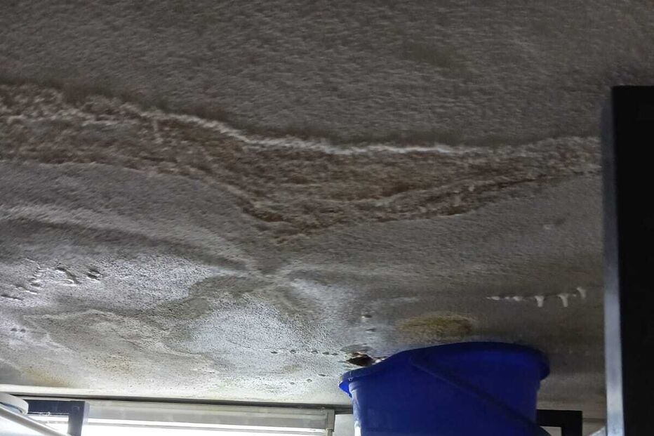 Infiltração no teto obriga ao uso de baldes para conter a água num armazém