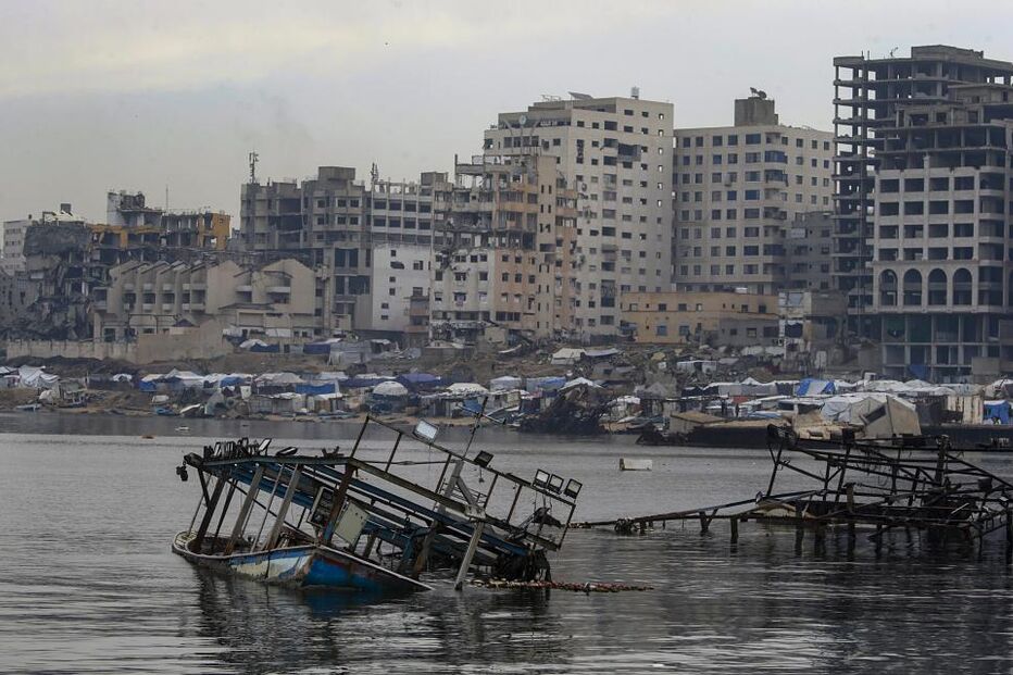 Destruição em Gaza após conflito, com prédios danificados e barcos naufragados