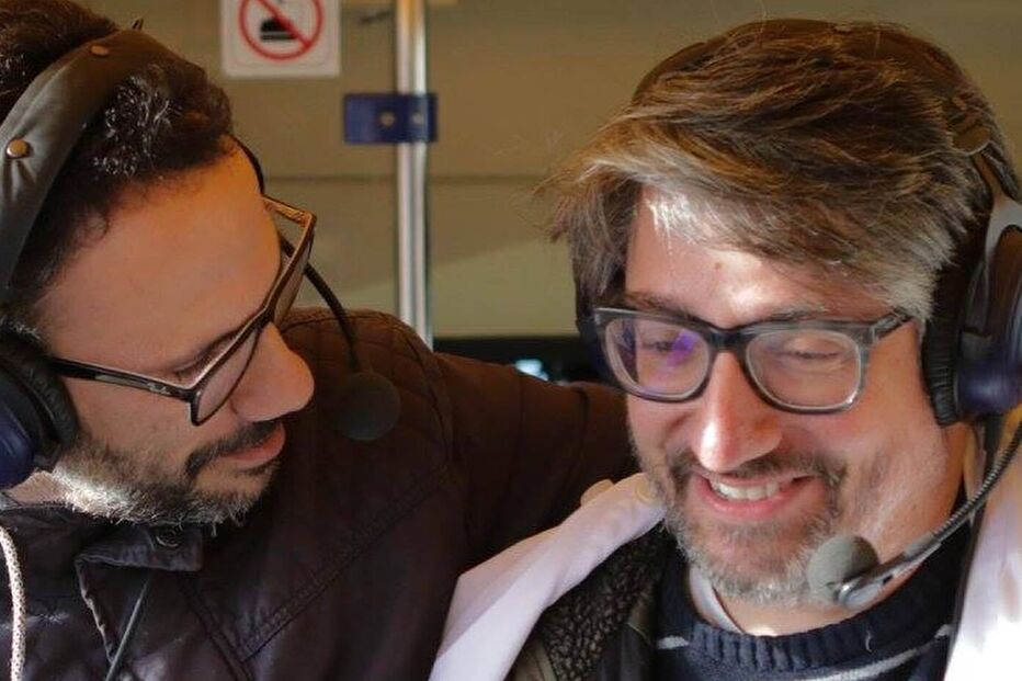 Dois homens de óculos e auscultadores sorriem