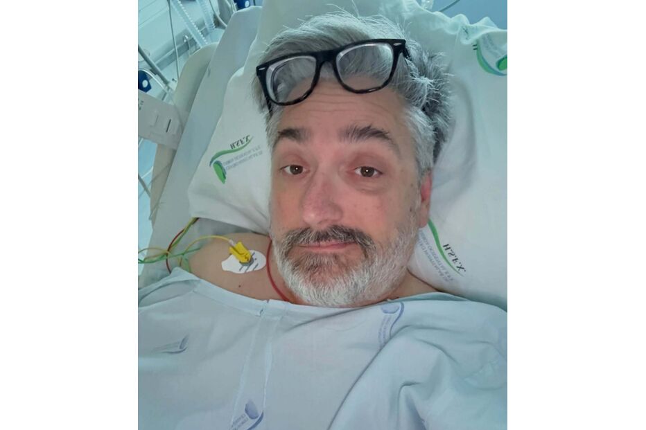 Homem de óculos numa cama de hospital com equipamento médico