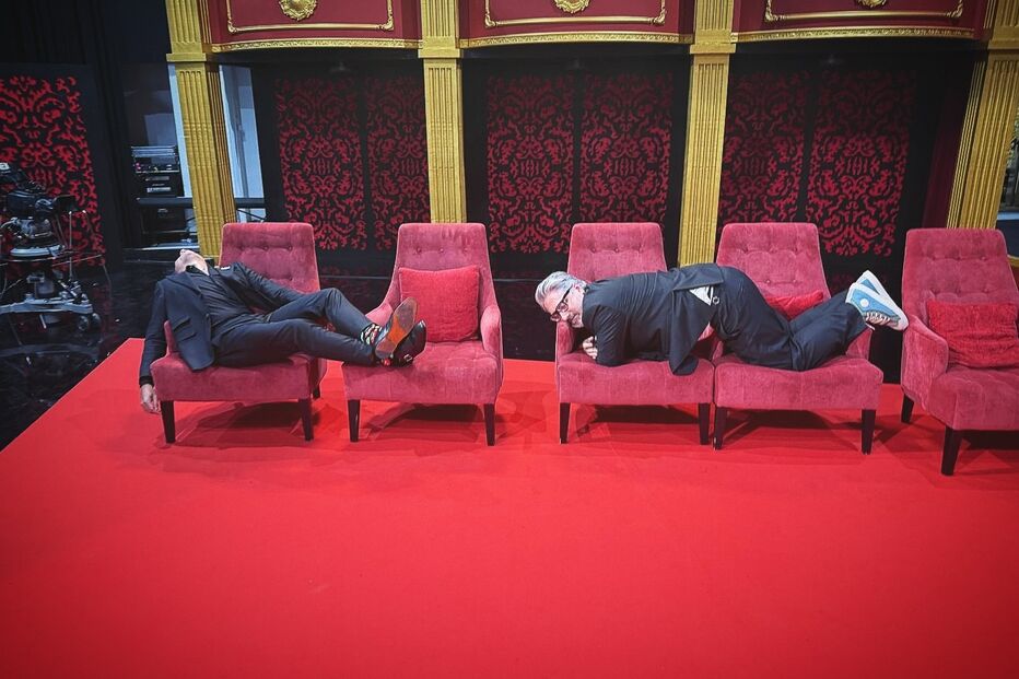 Dois homens em cadeiras num cenário de palco