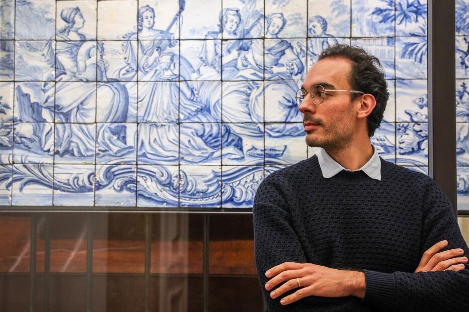 Homem posa junto a painel de azulejos em tons de azul e branco