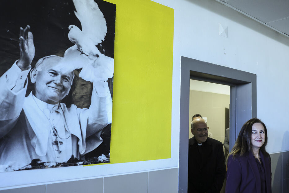 Um padre e uma mulher posam junto a um retrato de João Paulo II