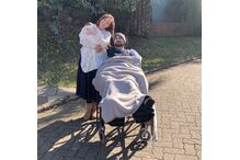 Mulher com bebé e homem em cadeira de rodas sorriem para a câmara