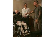 Homem em cadeira de rodas conversa com dois homens em ambiente interior