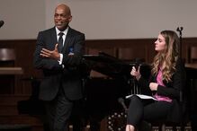 Um homem e uma mulher conversam com microfones em palco