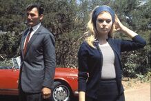 Brigitte Bardot e homem posam perto de carro vermelho