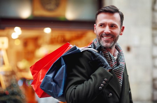 Homem sorri com sacos de compras na rua
