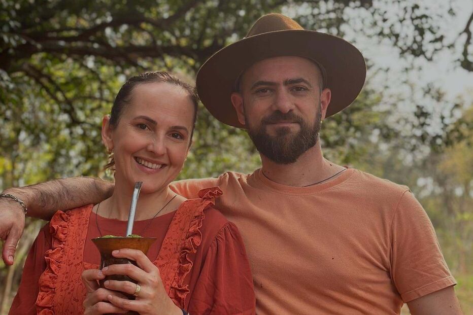 Um casal posa sorridente; mulher segura uma cuia de chimarrão