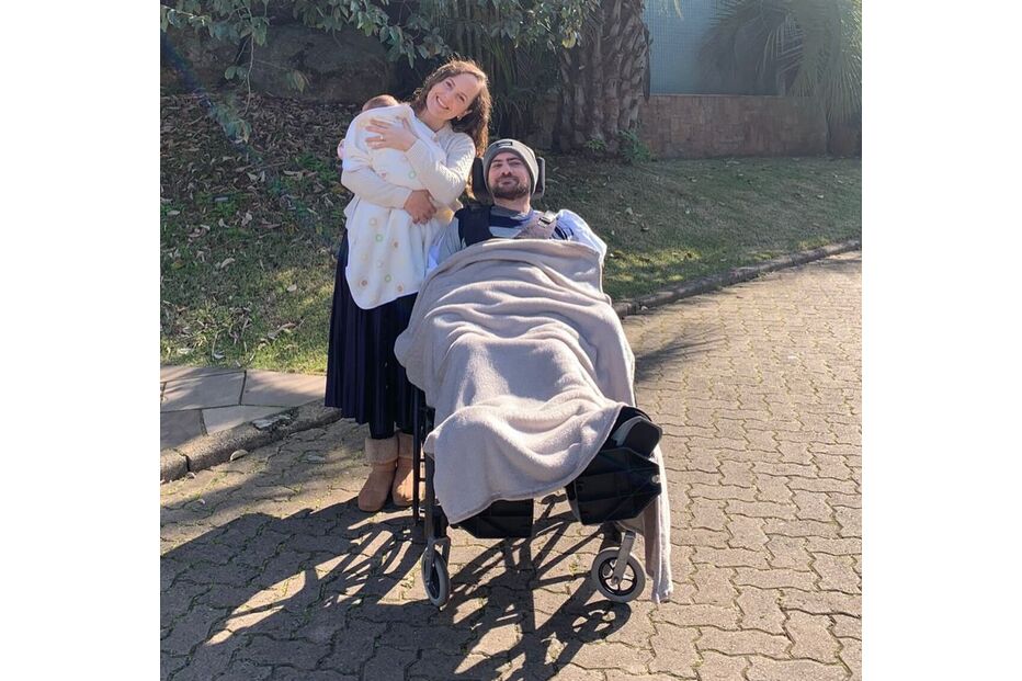 Mulher com bebé e homem em cadeira de rodas sorriem para a câmara