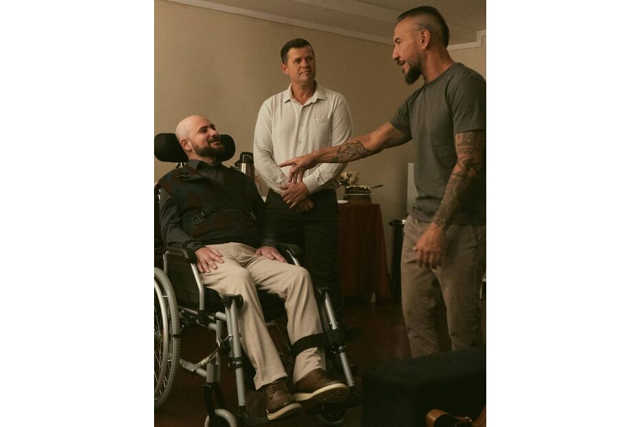 Homem em cadeira de rodas conversa com dois homens em ambiente interior