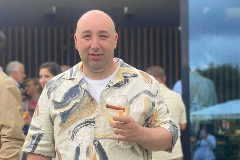 Um homem sorri enquanto segura uma bebida num evento