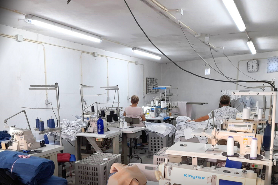 Interior de fábrica têxtil com máquinas de costura e duas pessoas a trabalhar