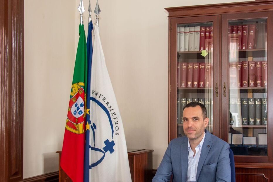 Homem sentado à secretária com as bandeiras de Portugal e da Ordem dos Enfermeiros